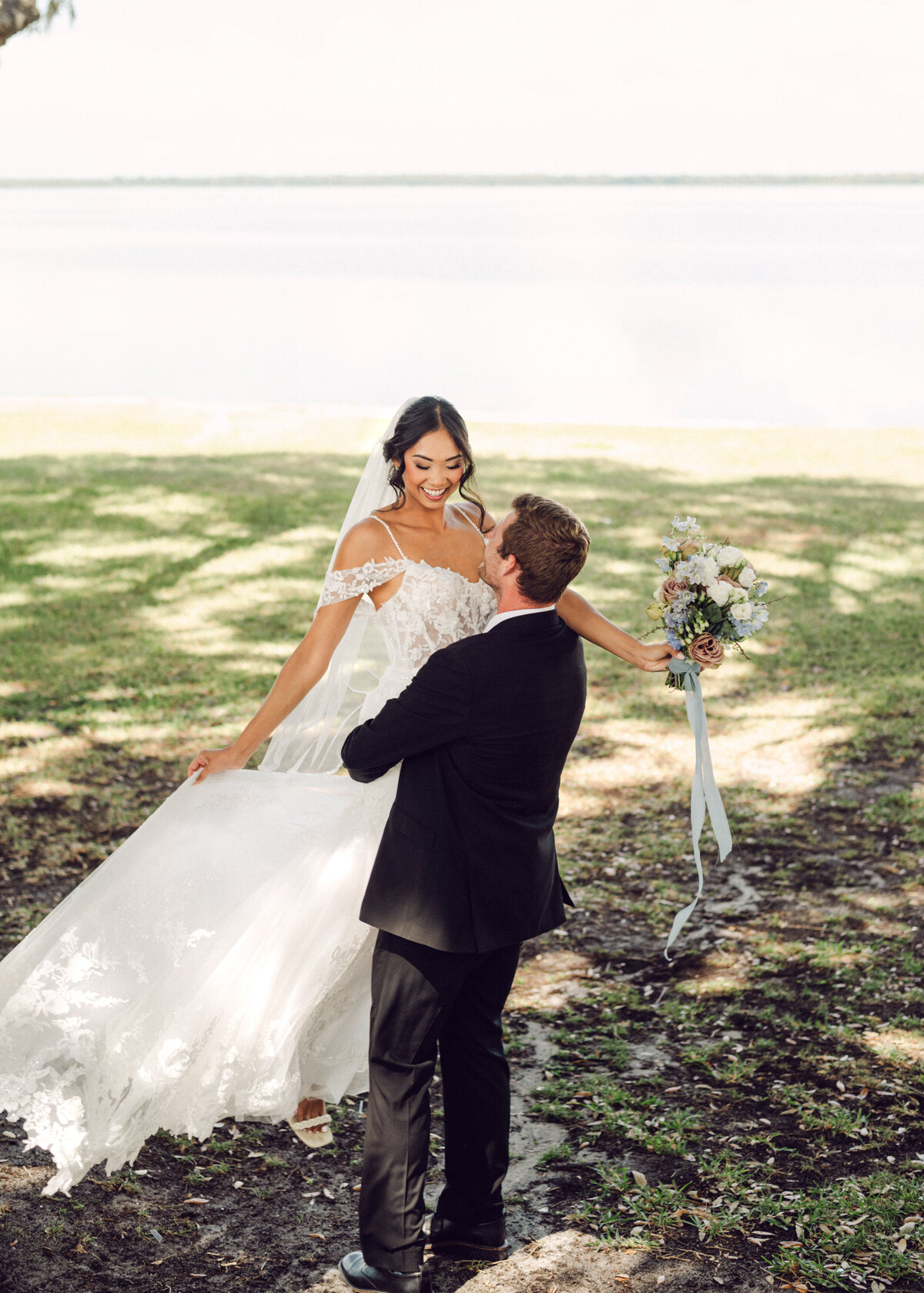 groom picks up bride and spins her around by the water venue Bella Cosa Lake  Whales  Florida