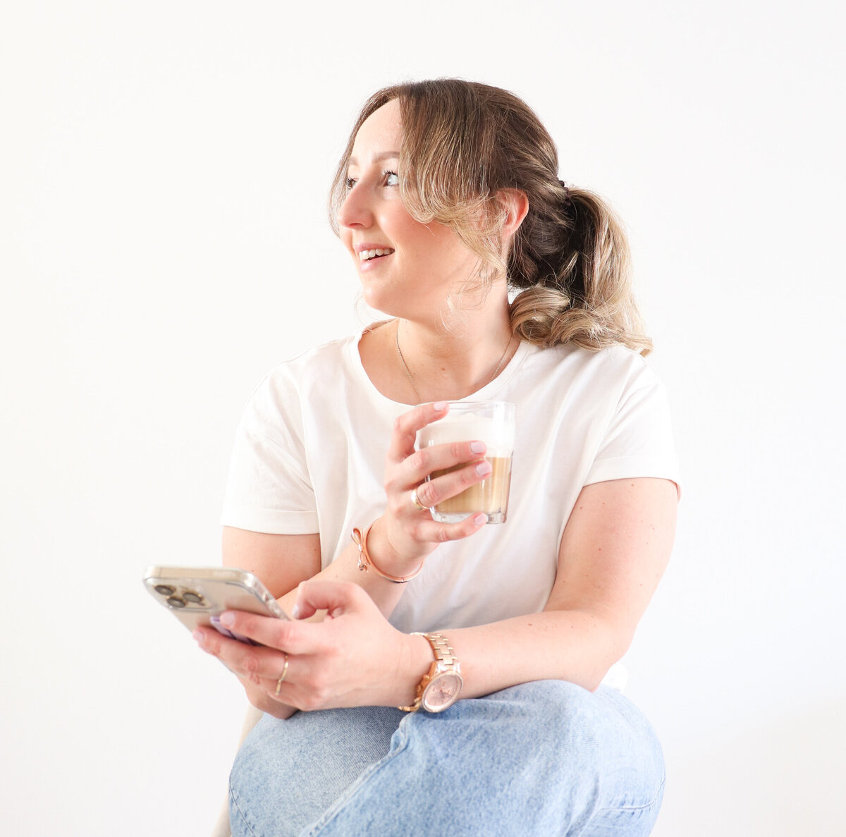 vrouw in wit t-shirt met koffie en een mobiele telefoon in haar hand