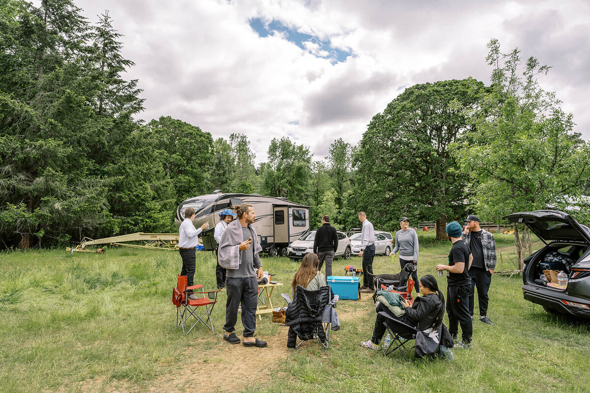 A group of people outdoors with camper and trees in the background.