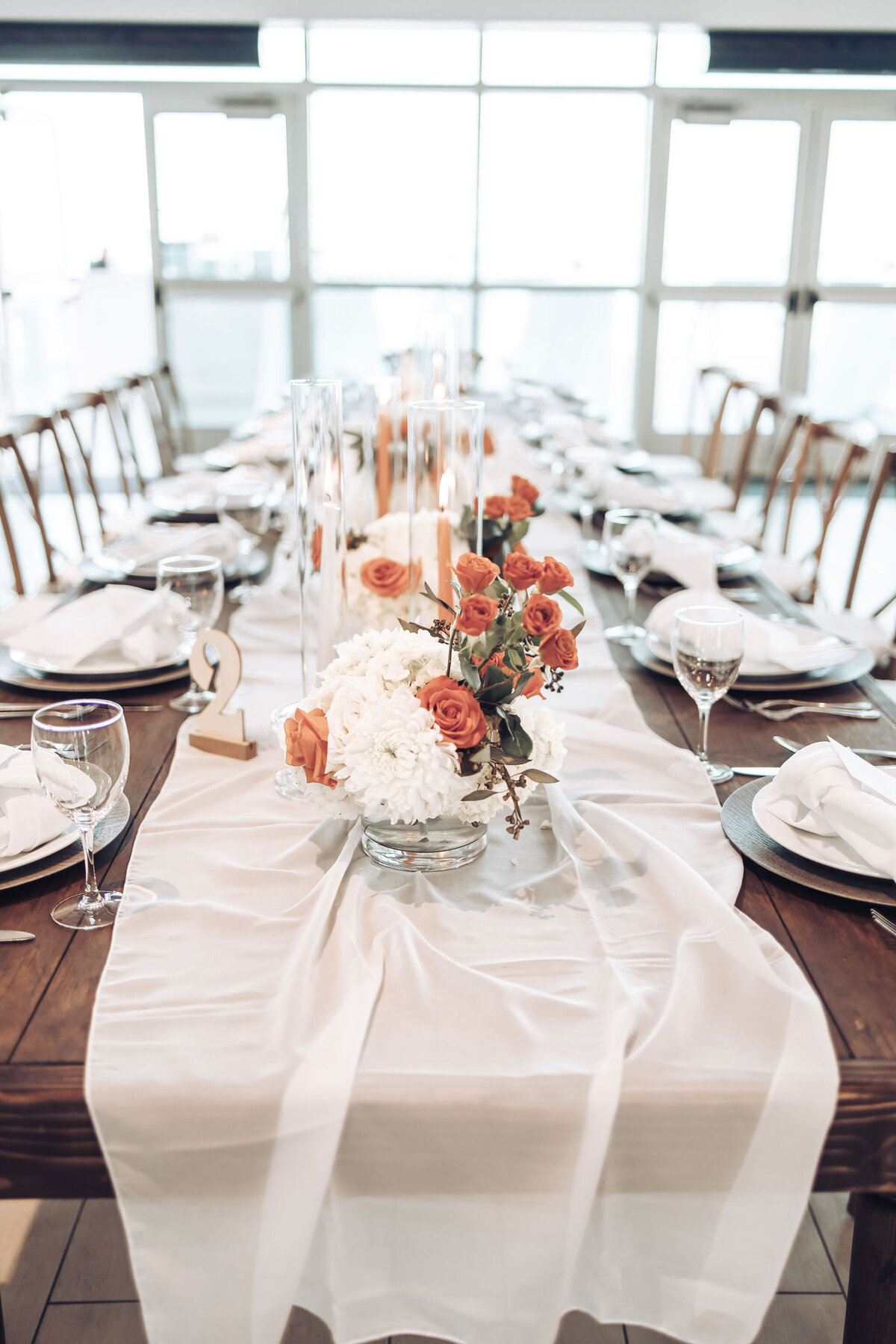 table runner with a white cloth, orange and white flowers, and candles