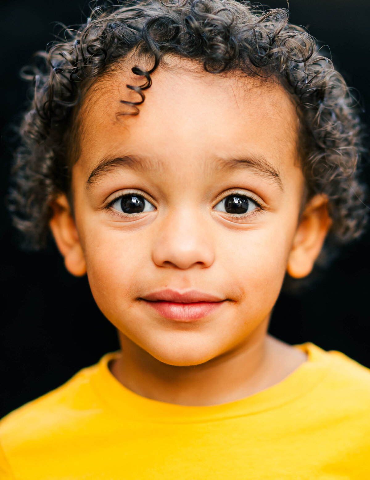 Toddler boy smiling warmly against a black backdrop — fine art portrait by S. Reed Photography