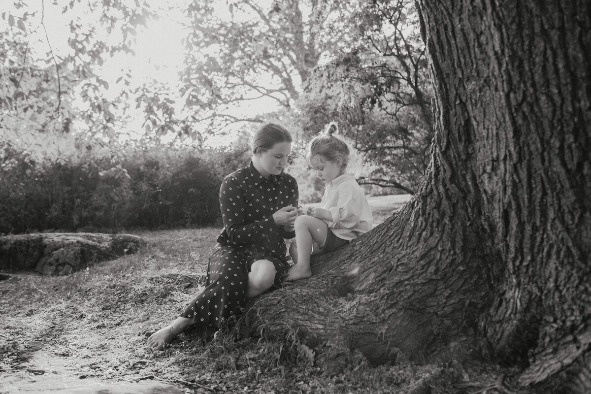 Perhekuva äidistä ja hänen 3-vuotiaasta pojasta istumassa puun rungossa puistossa Helsingissä