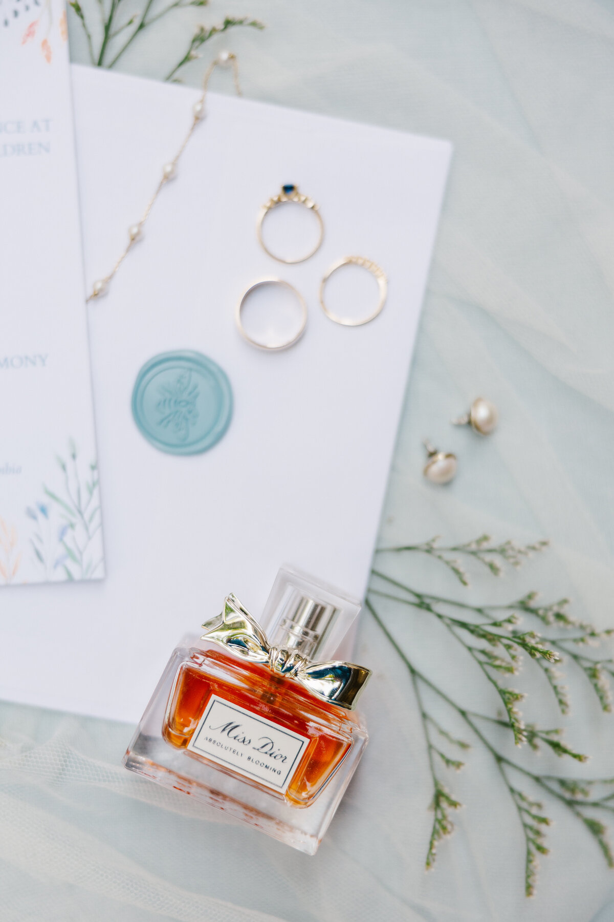 Flat lay of wedding stationery, wedding rings, and a perfume bottle