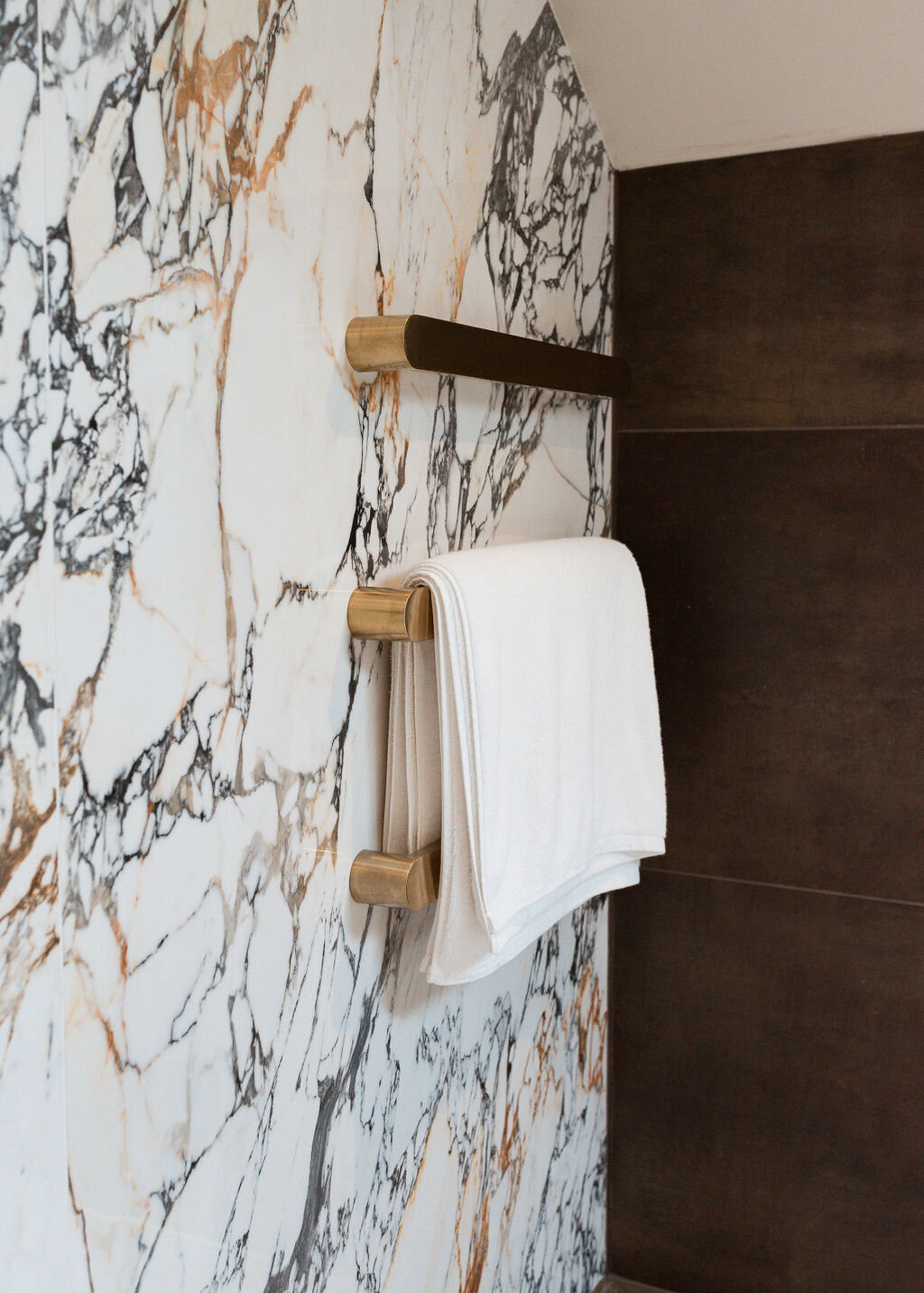 Modern gold towel bars mounted on a white marble wall with black veining.