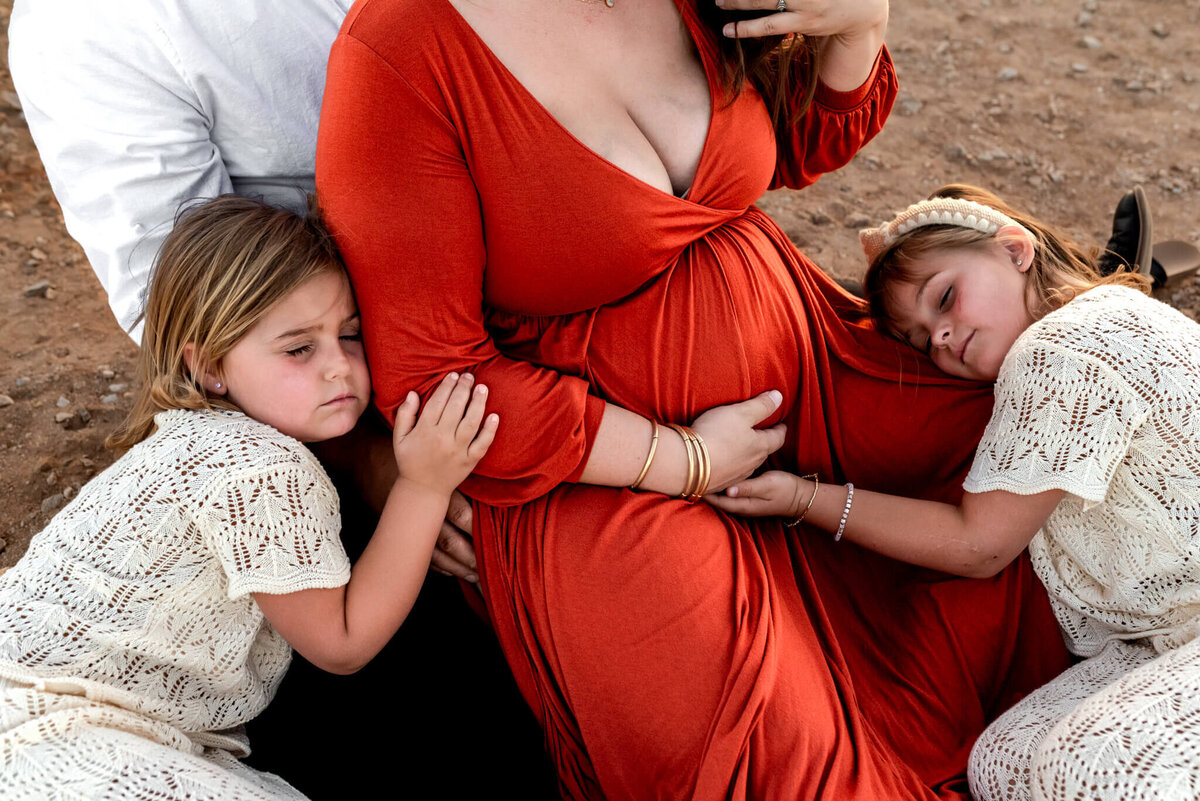 Daughters lie on mom while hugging her and their sibling-to-be for Arizona maternity photo