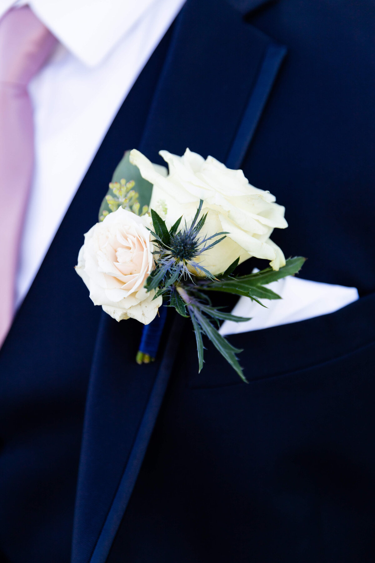 Boutannaire of white roses against navy blue suit