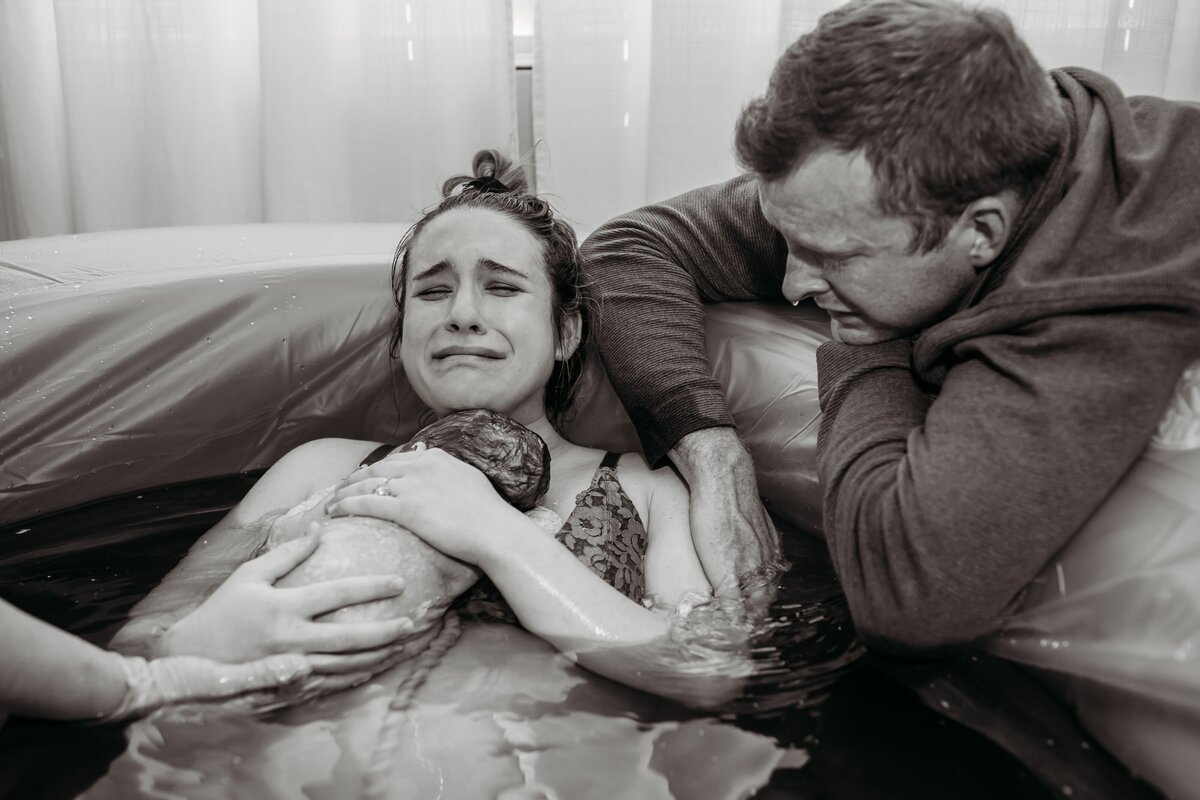 new mom cradles newborn baby as emotional dad looks on immediately after home waterbirth in Charlotte, NC. Photography by Nicole Bertrand