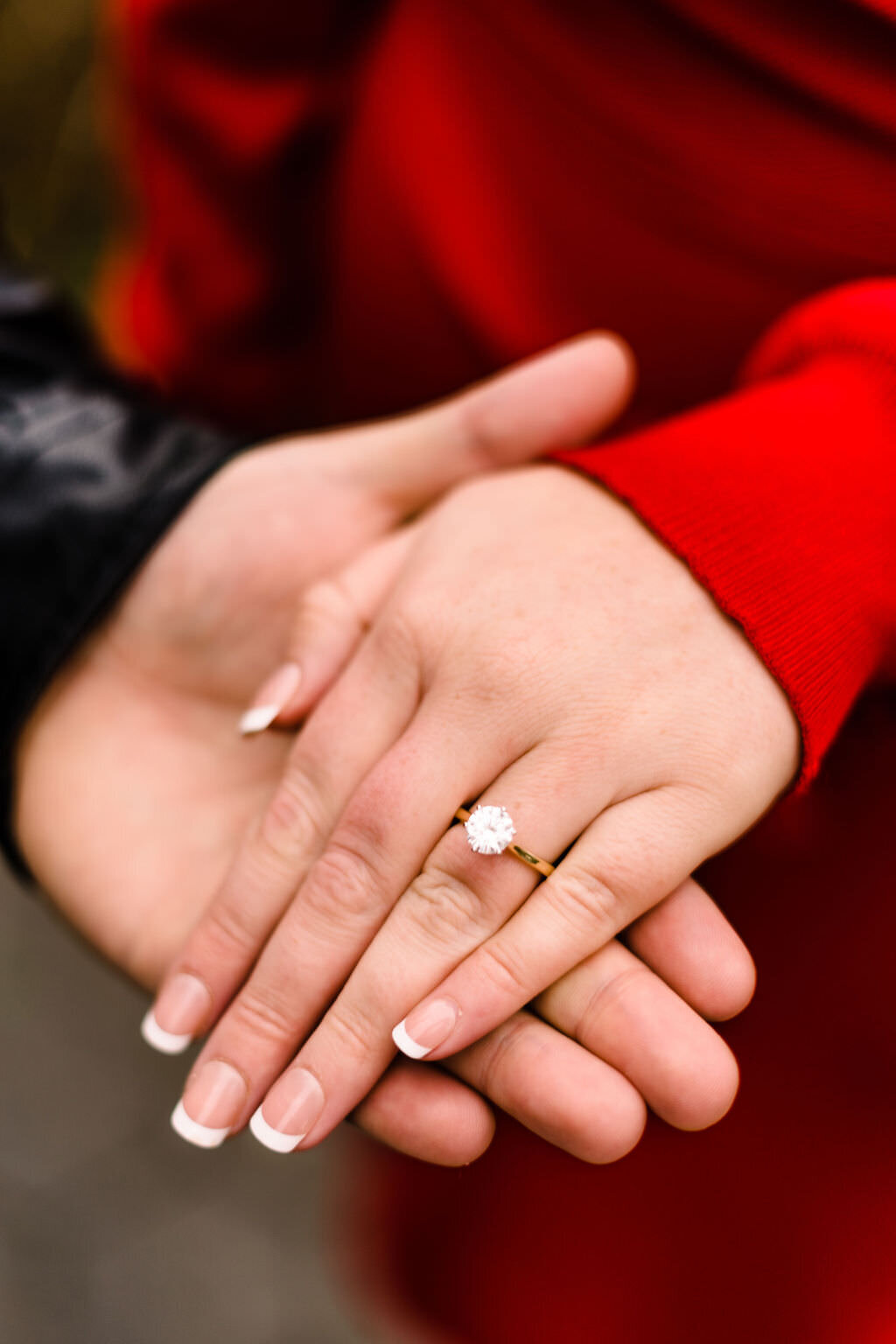 person's hand holding up another as it shows off an engagement ring