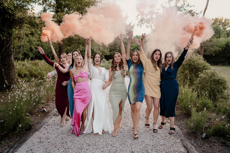 Photo de groupe de la mariée avec ses amies tenant des fumigènes colorés au Domaine de Petiosse, lors d’un mariage capturé en duo photo et vidéo.