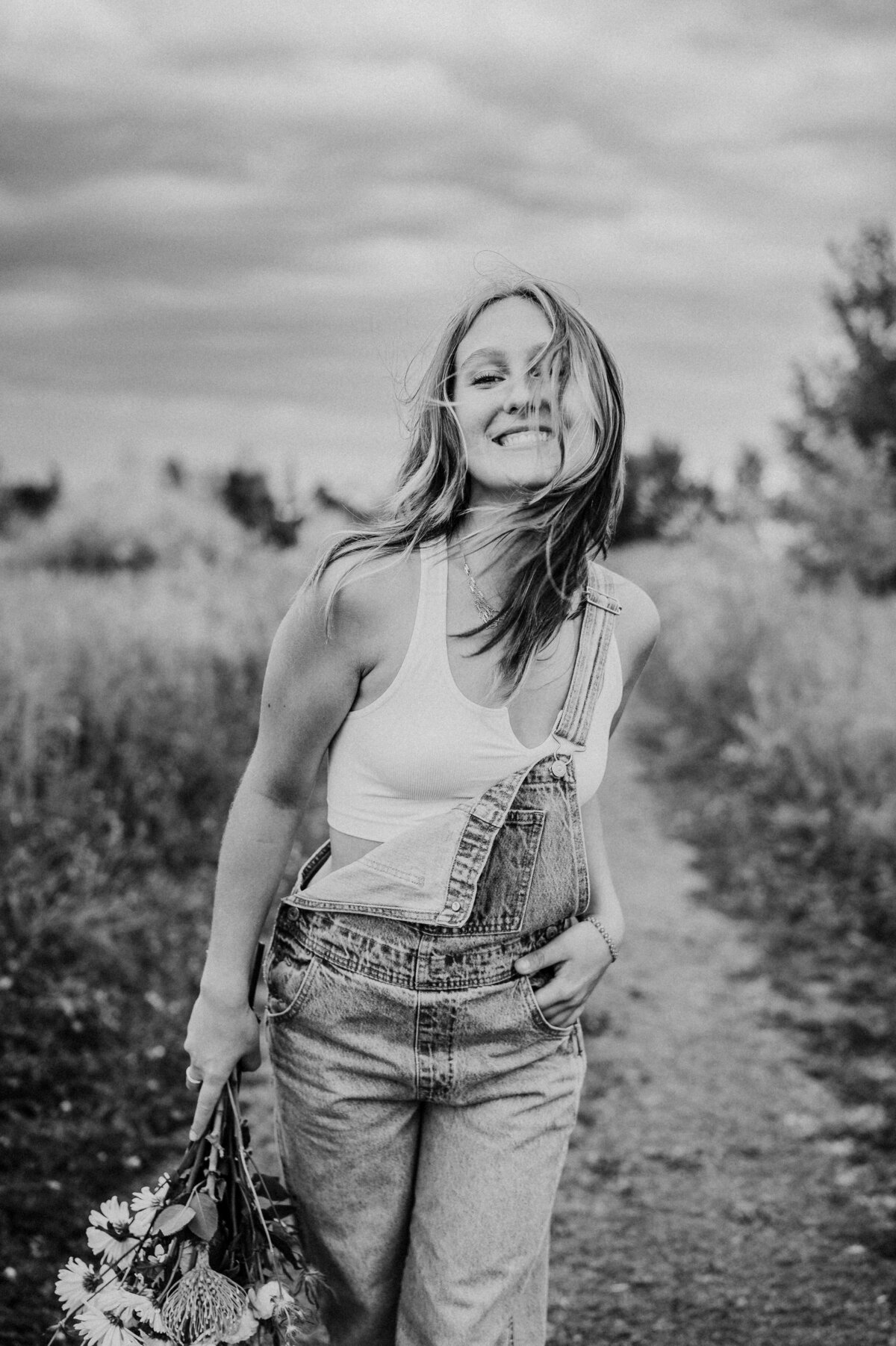 Black and white fun and energetic senior portrait of her walking on a dirt trail outside