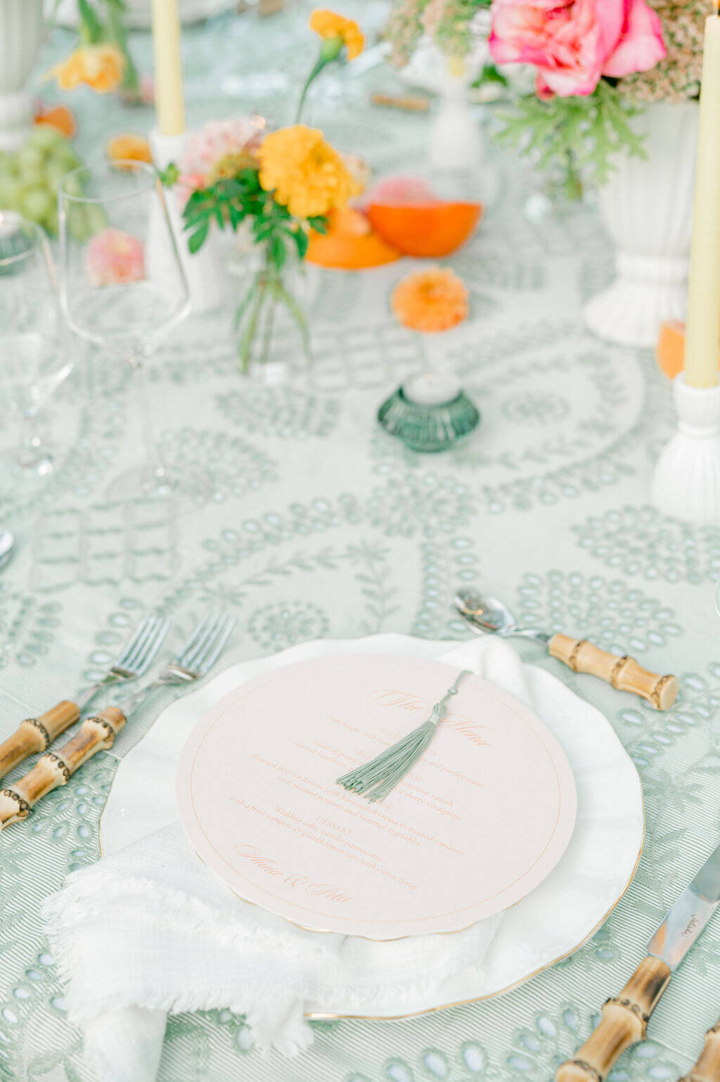 Elegant wedding day stationery with tassel menu atop white plate and bamboo cutlery.