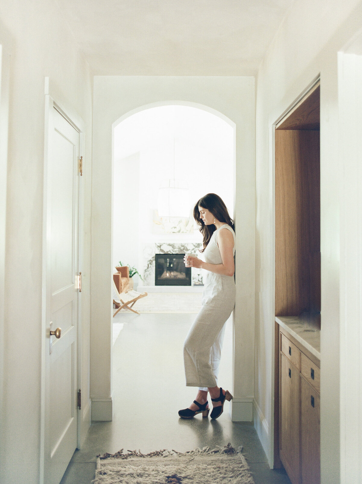 relaxed, natural designer in linen jumpsuit with coffee, under arch at Fernhaus, Northern michigan