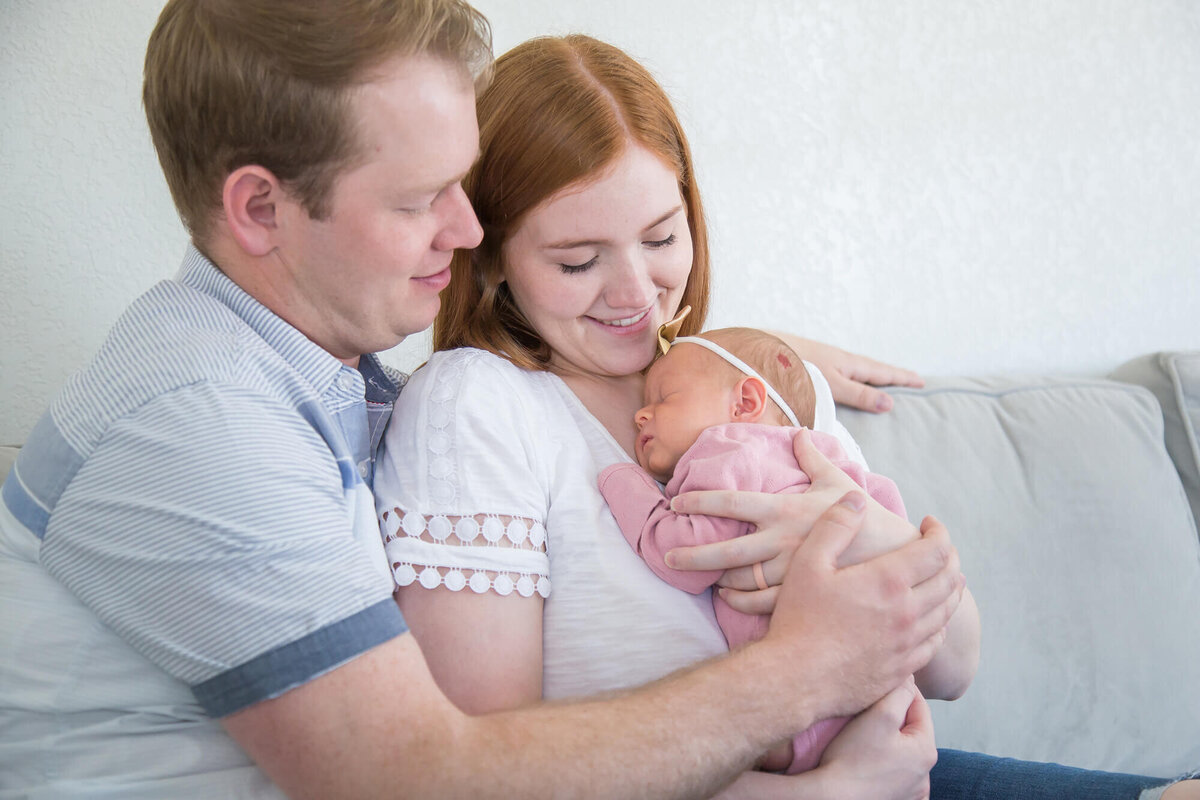 joyful couple snuggling newborn baby girl close and looking at her lovingly