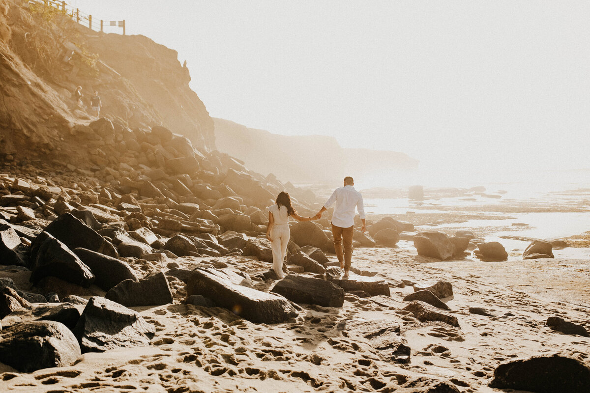 Man and woman in white walking down rocky beach