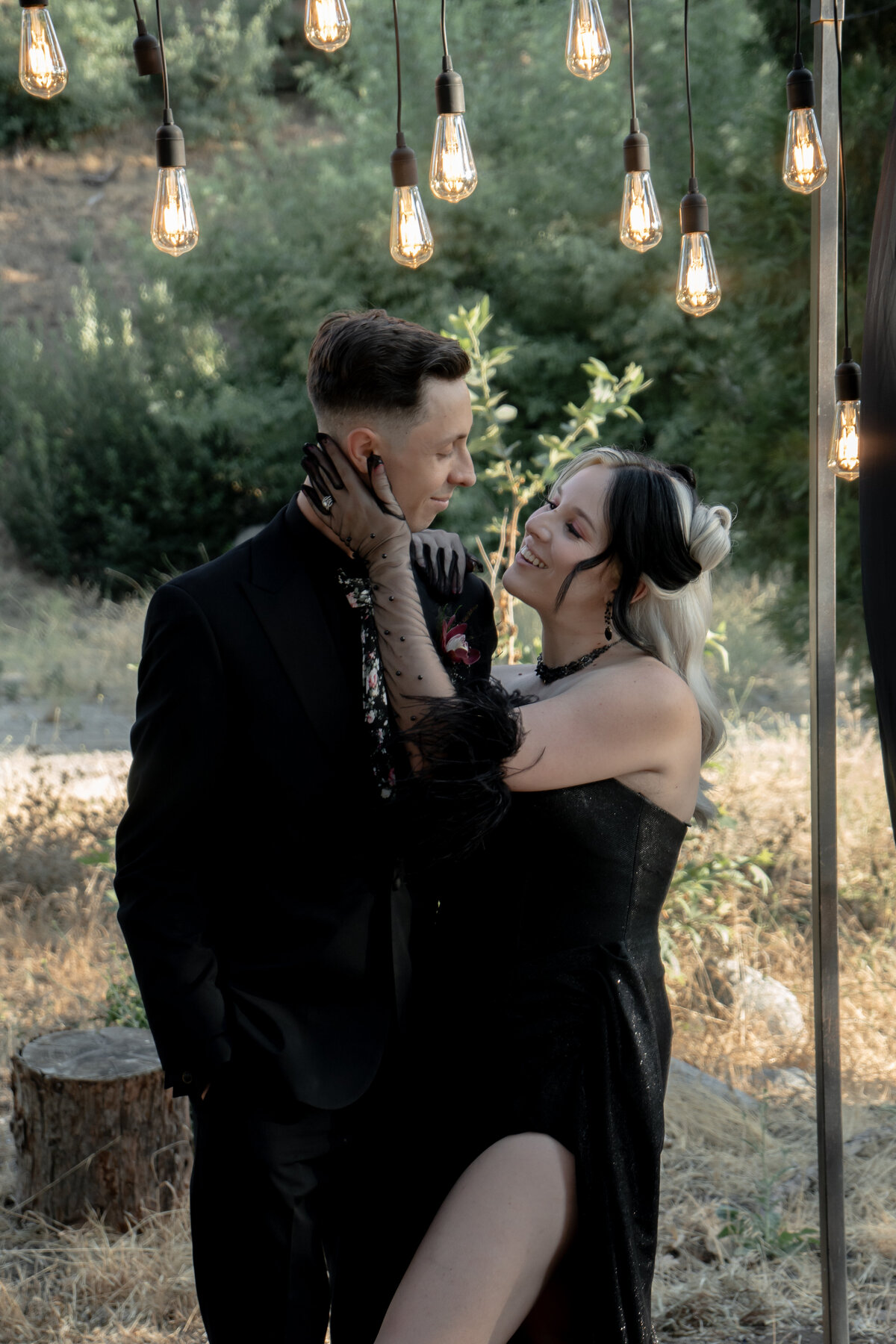 Bride and groom in mountains of Oak Glen California during golden hour with the bride caressing the grooms cheek in their goth attire.