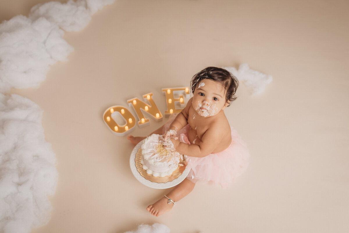 one year old baby girl at atlanta ga cake smash portrait studio wearing a pink tutu and smashing and eating a cake  at marietta, ga maternity and newborn portrait studio