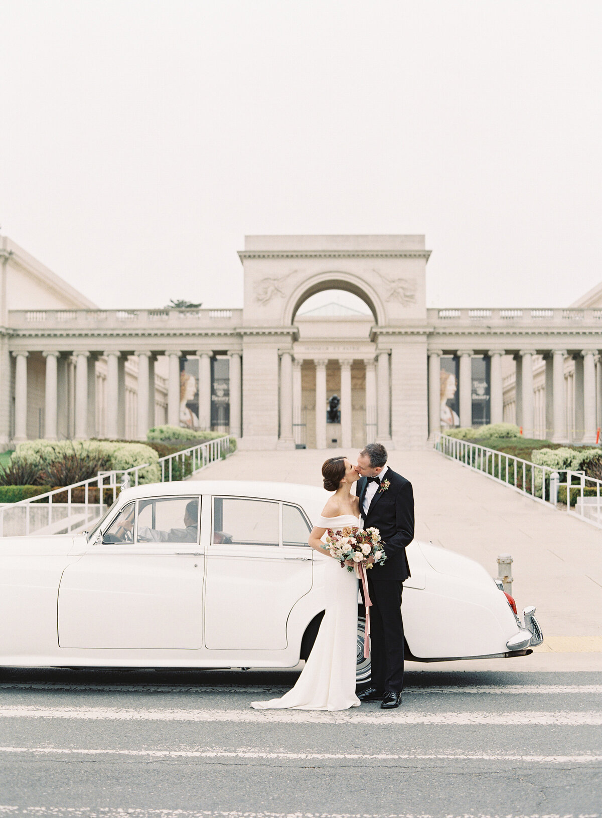 A stunning moment of a bride and groom posing with a vintage car on their wedding day at the iconic Legion of Honor in San Francisco. The timeless elegance of the classic car and the grand architecture of the venue perfectly capture the charm and sophistication of San Francisco wedding photography