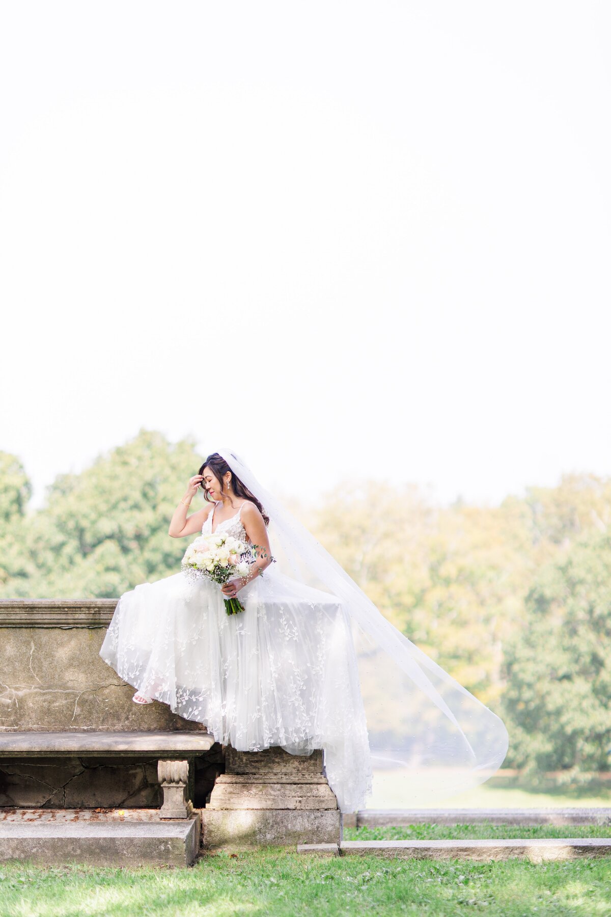 Bride sitting with her wedding dress blowing in the breeze during her Boston bridal portraits