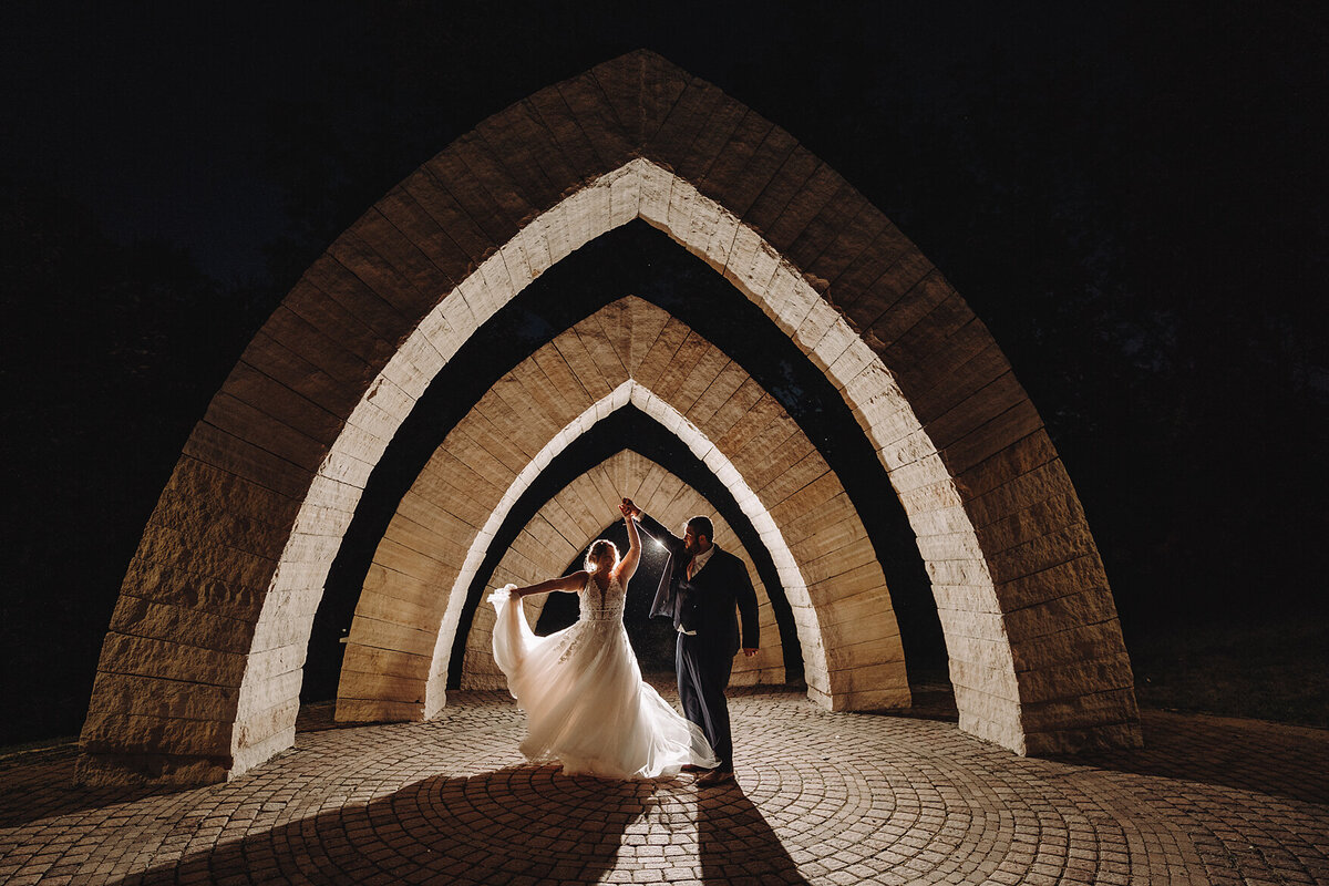 Bride twirling in chic gown beside groom night time shot at celebrations farms in iowa city