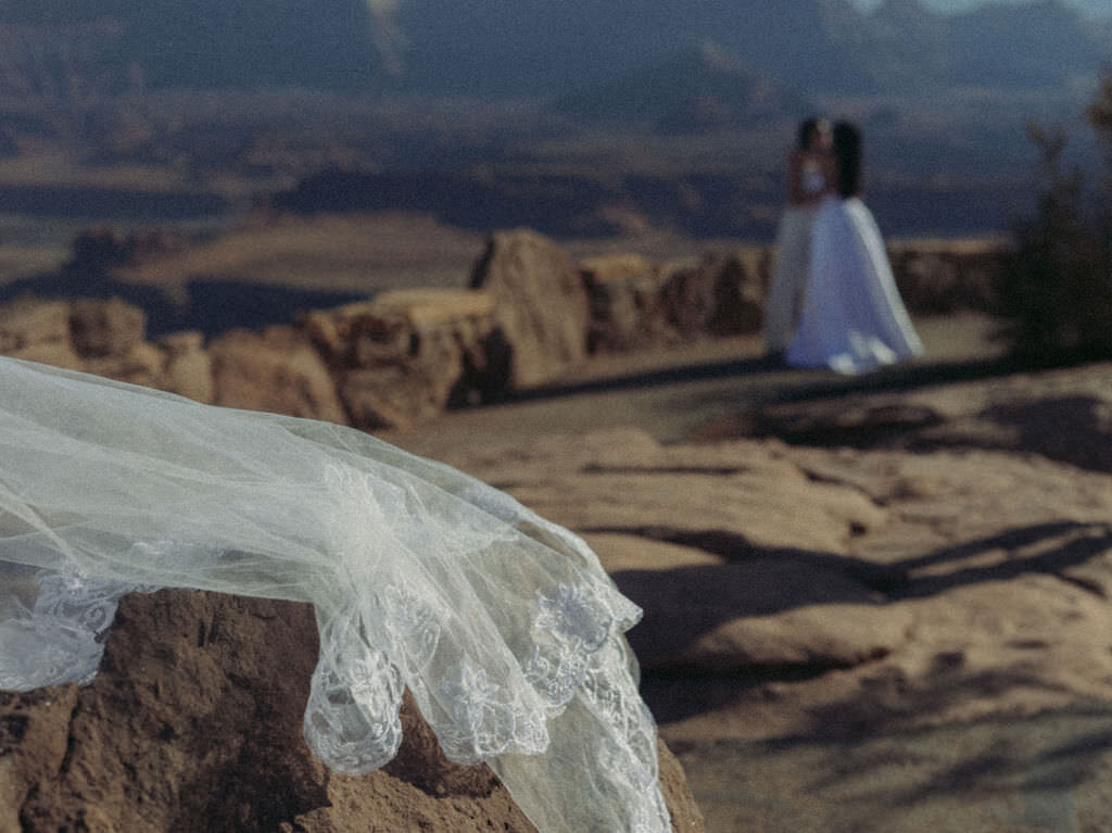 A veil on a rock with a wedding couple kissing in the distance