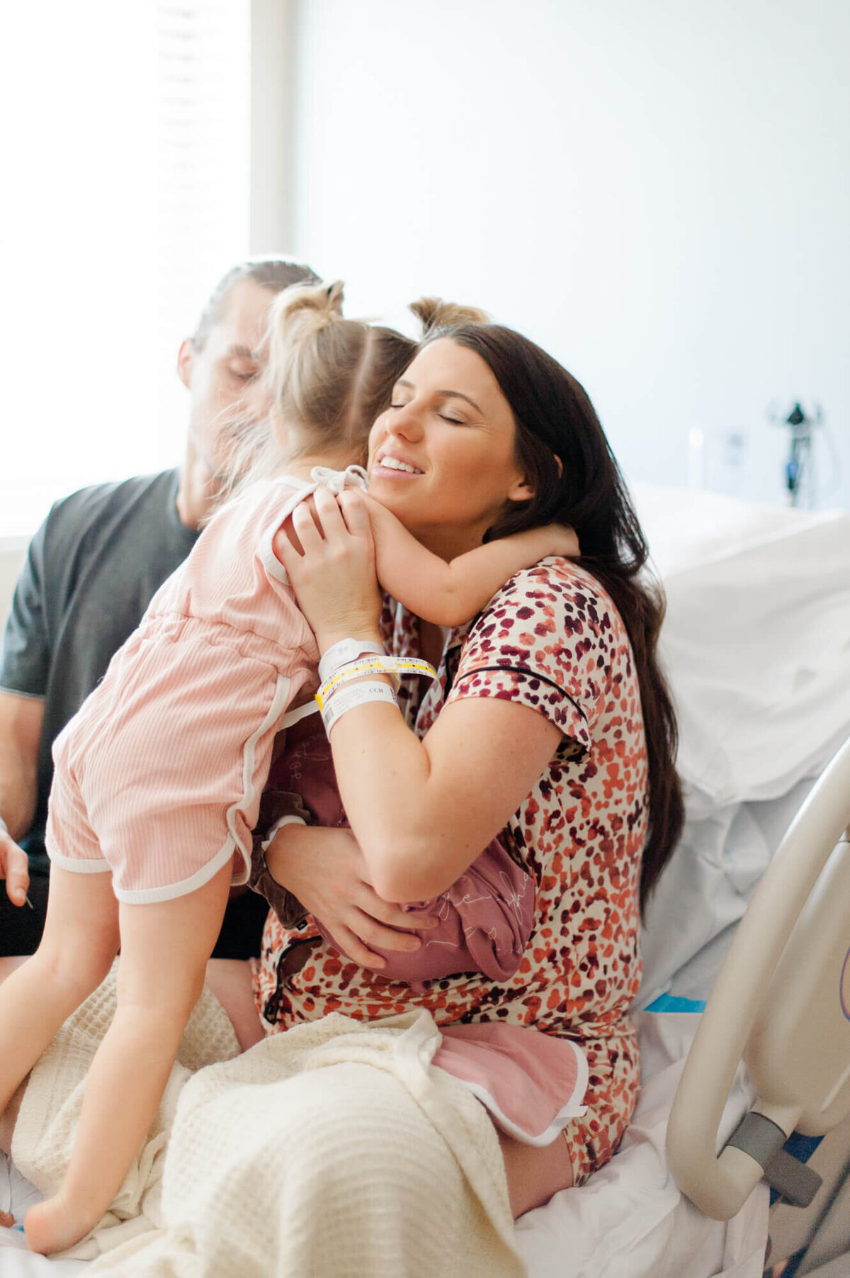 Toddler hugging mom as she joins family at the hospital after her little sister was born