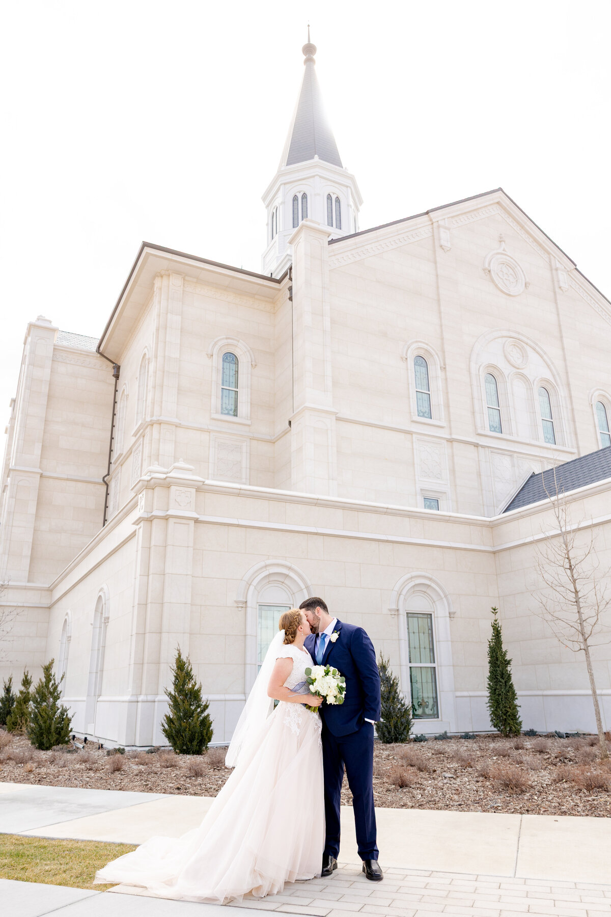 A romantic shot of the bride and groom sharing a kiss in front of the towering spire of the LDS temple.