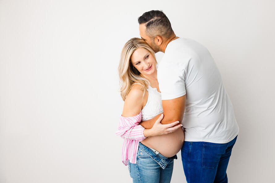 A man kisses his pregnant wife in a photography studio.