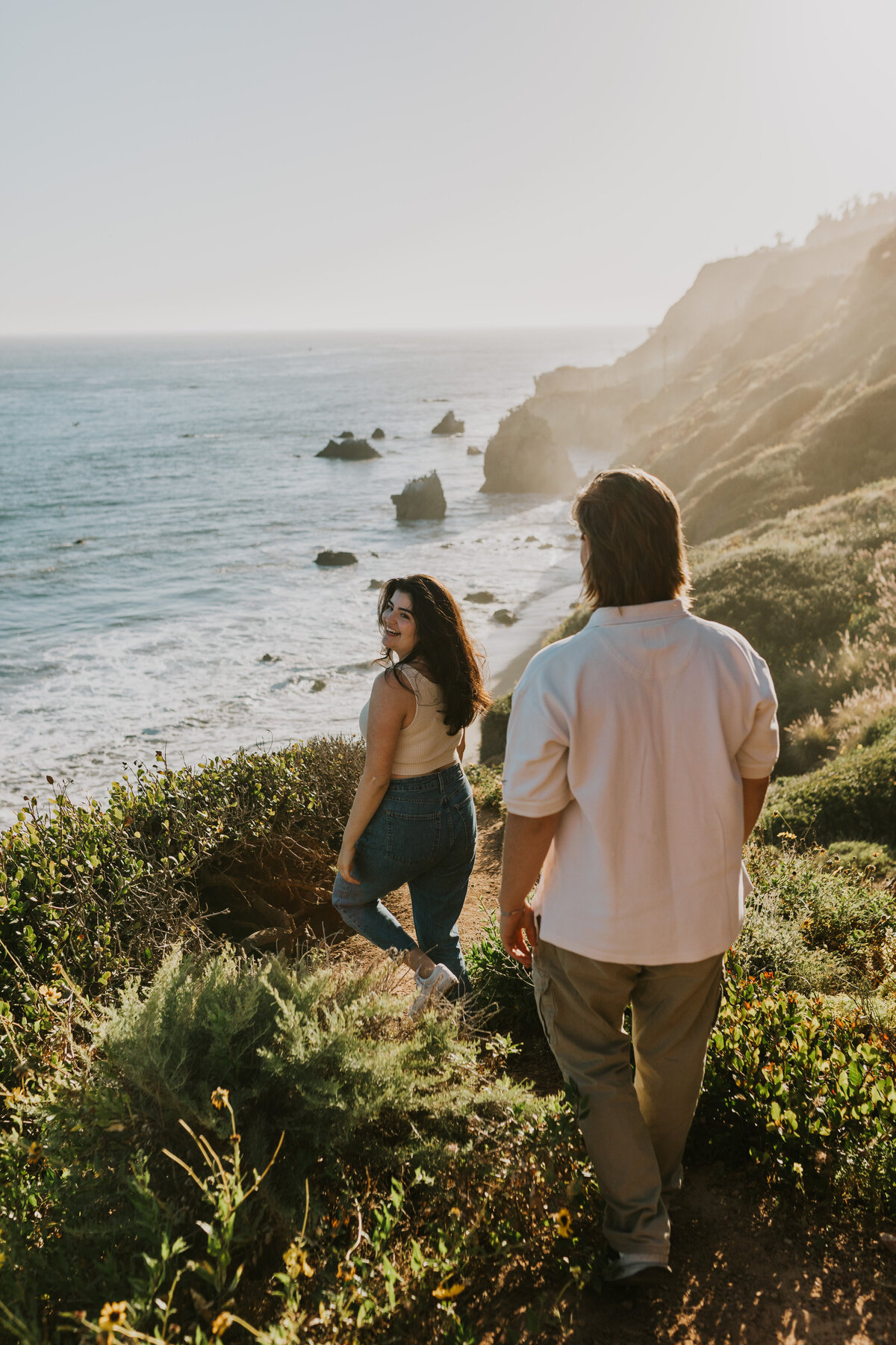 Couple walking hand-in-hand along ocean cliffs, Indiana adventure engagement.