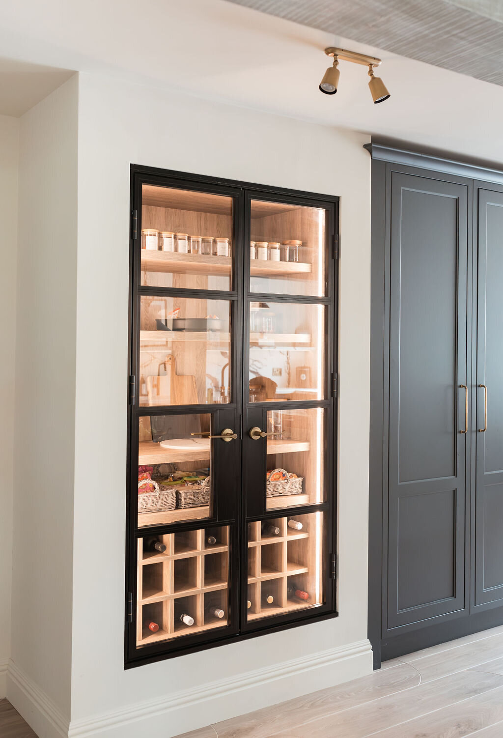 Built-in pantry cabinet with glass doors with black frames. Pantry has lighting inside to emit a soft, warm glow.