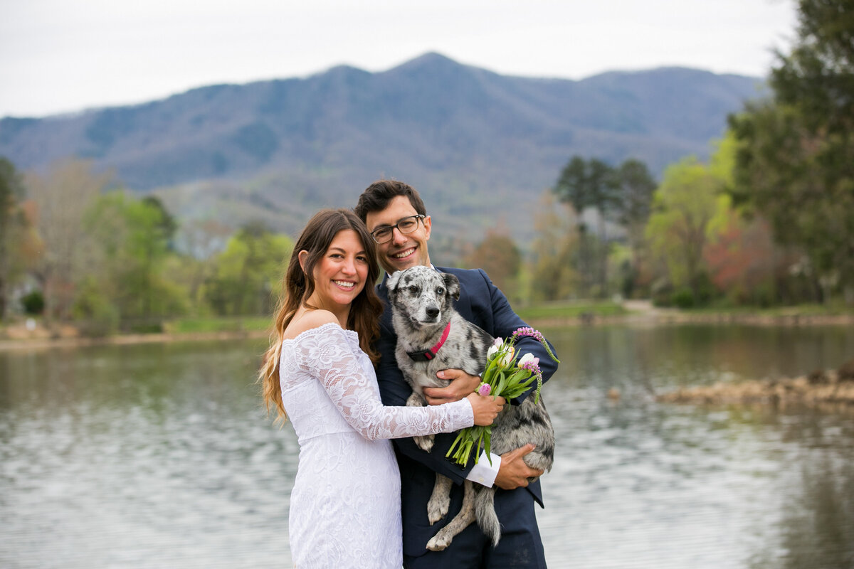 couple smiles at Lake Tomahawk in Black Mountain while they hold their dog