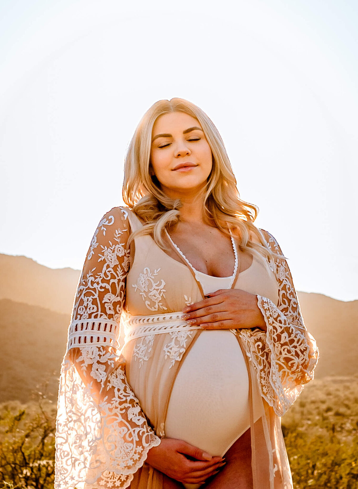 mom-to-be posing in lace dress with hands on her belly for pregnancy session in Arizona with her photographer