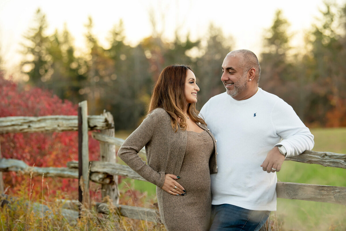 up-close photo of husband and wife leaning against a fence for their outdoor fall maternity photography session in Burlington