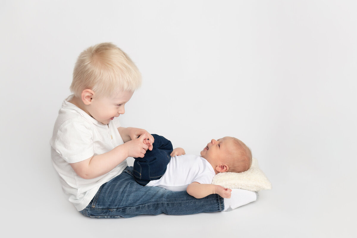 Heartwarming moment of a toddler meeting his newborn sibling, photographed on a clean white background in studio by Meraki Photographic Creations. Captured in-studio at Meraki Photographic Creations in Paris, Ontario.