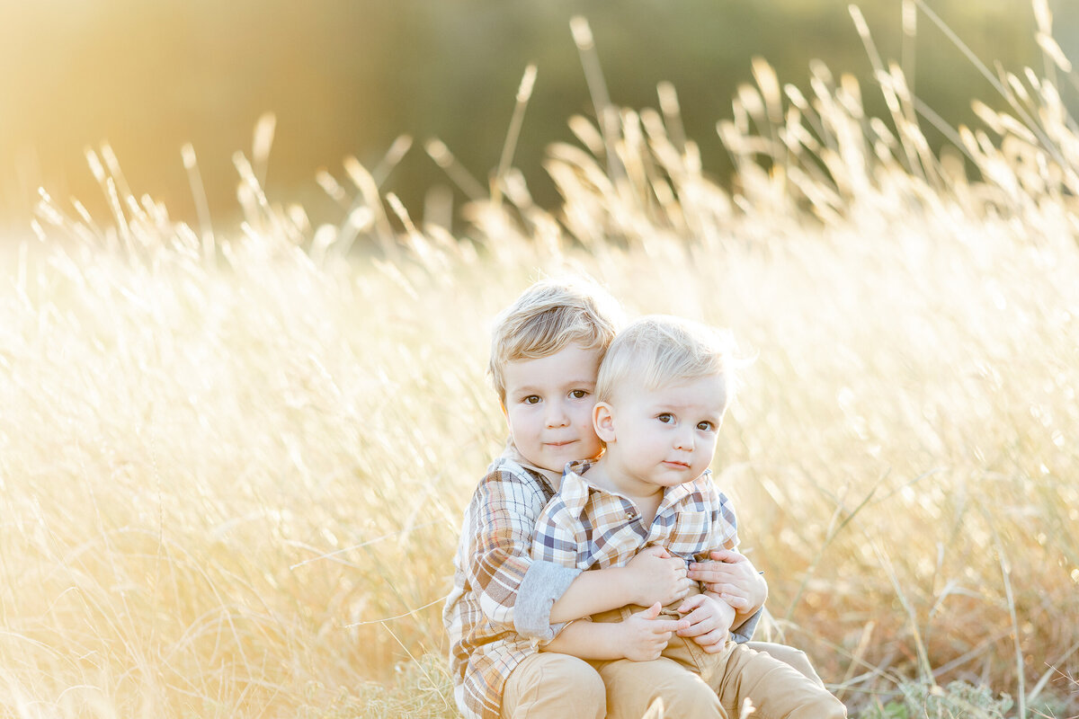 Two young brothers sitting together in the grass at a Dallas park.