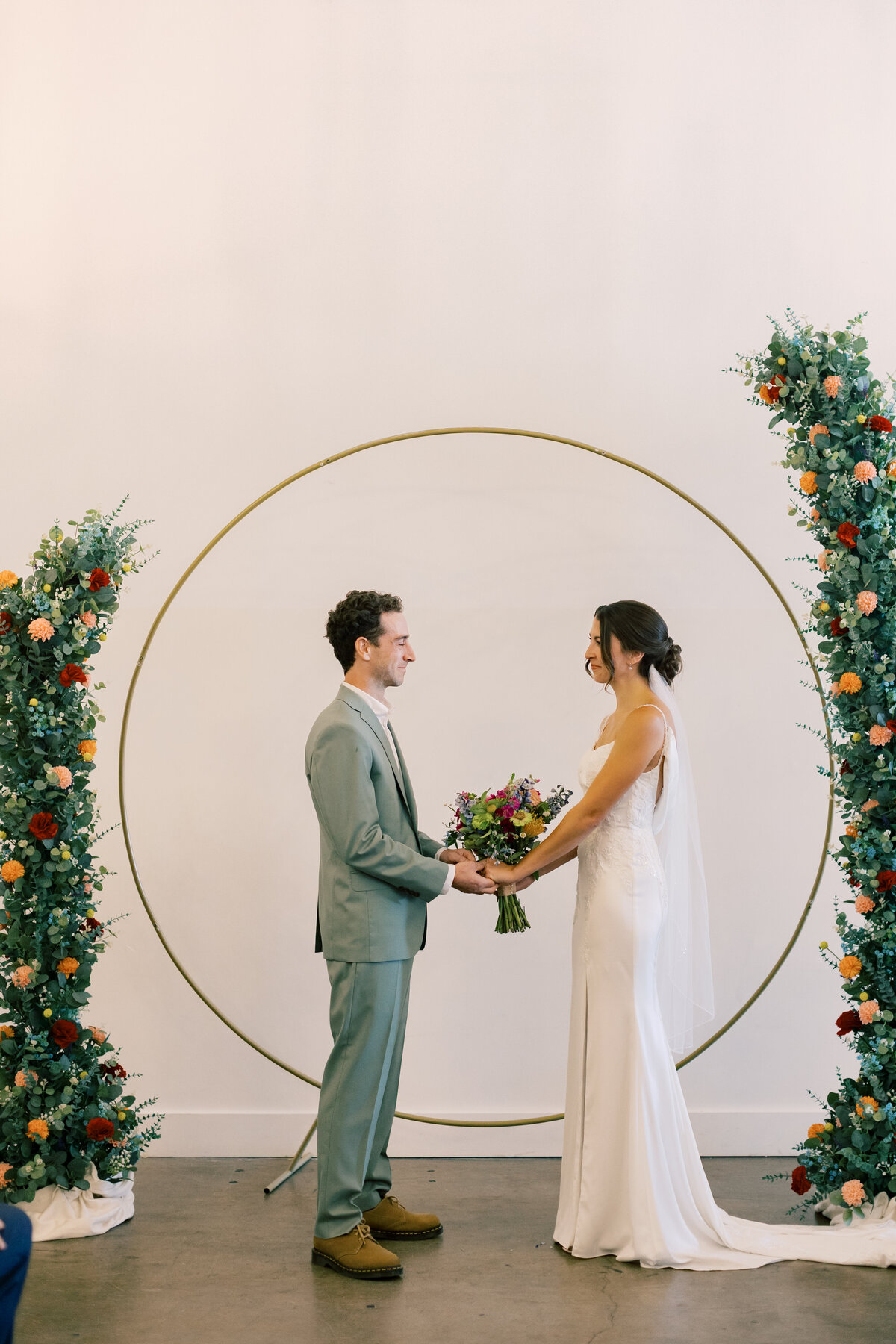 Round gold ceremony arch decorated with colorful flowers by Crimson & Clover at Brendan and Sara’s Fetewell wedding ceremony.
