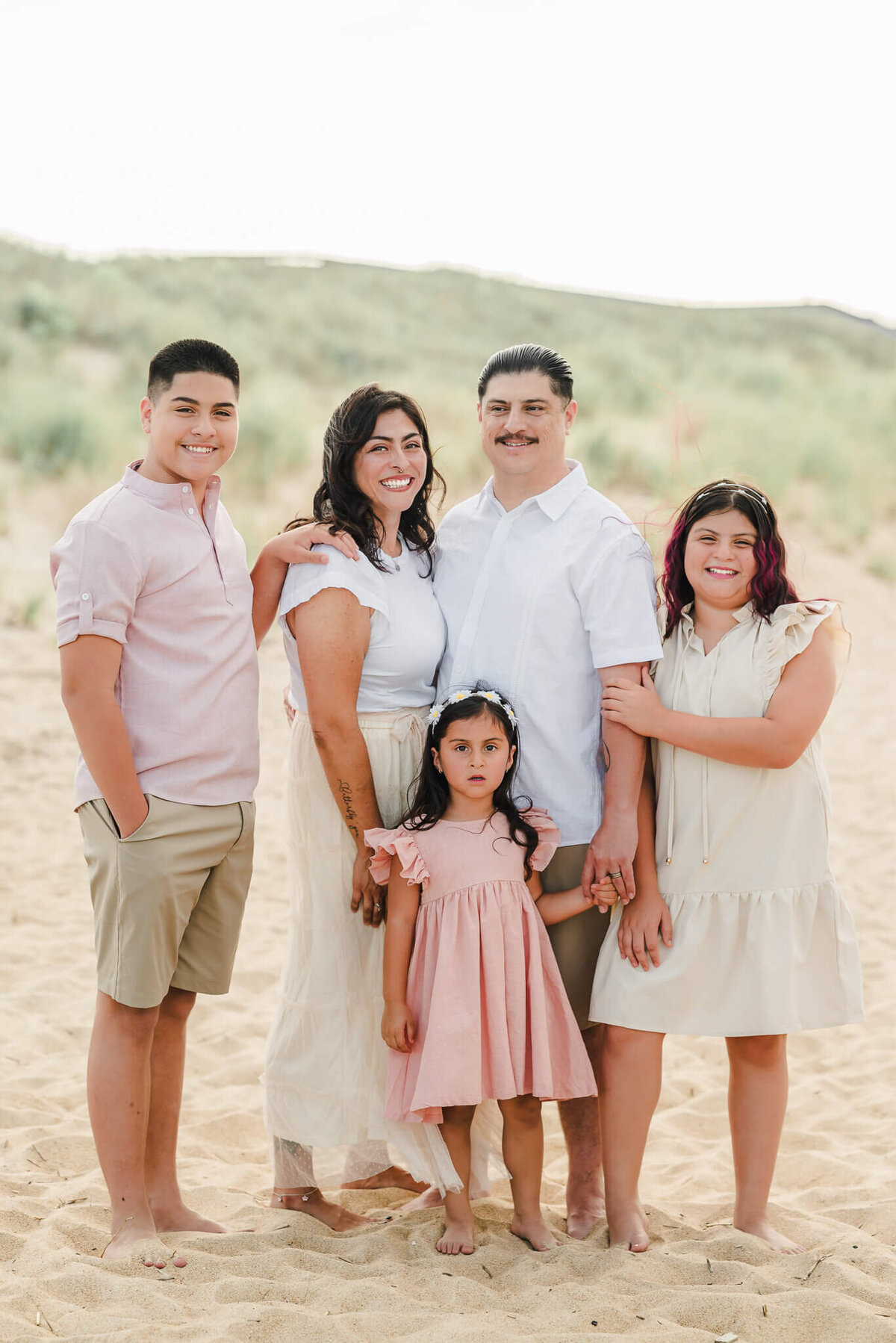 A family of five poses near the dunes at Fort Story Beach in Virginia Beach. Everyone is dressed in khaki and white or khaki and pink.