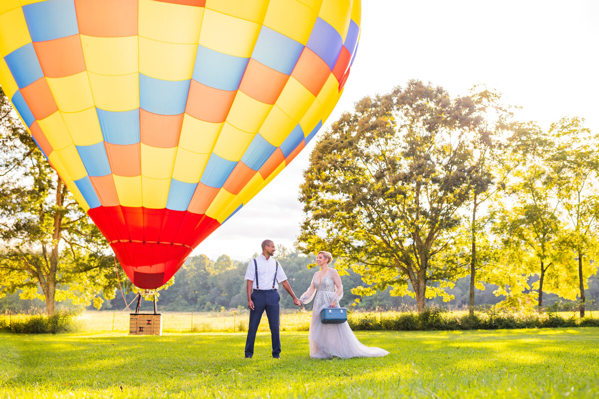 Couple holds hands under colorful hot air balloon.