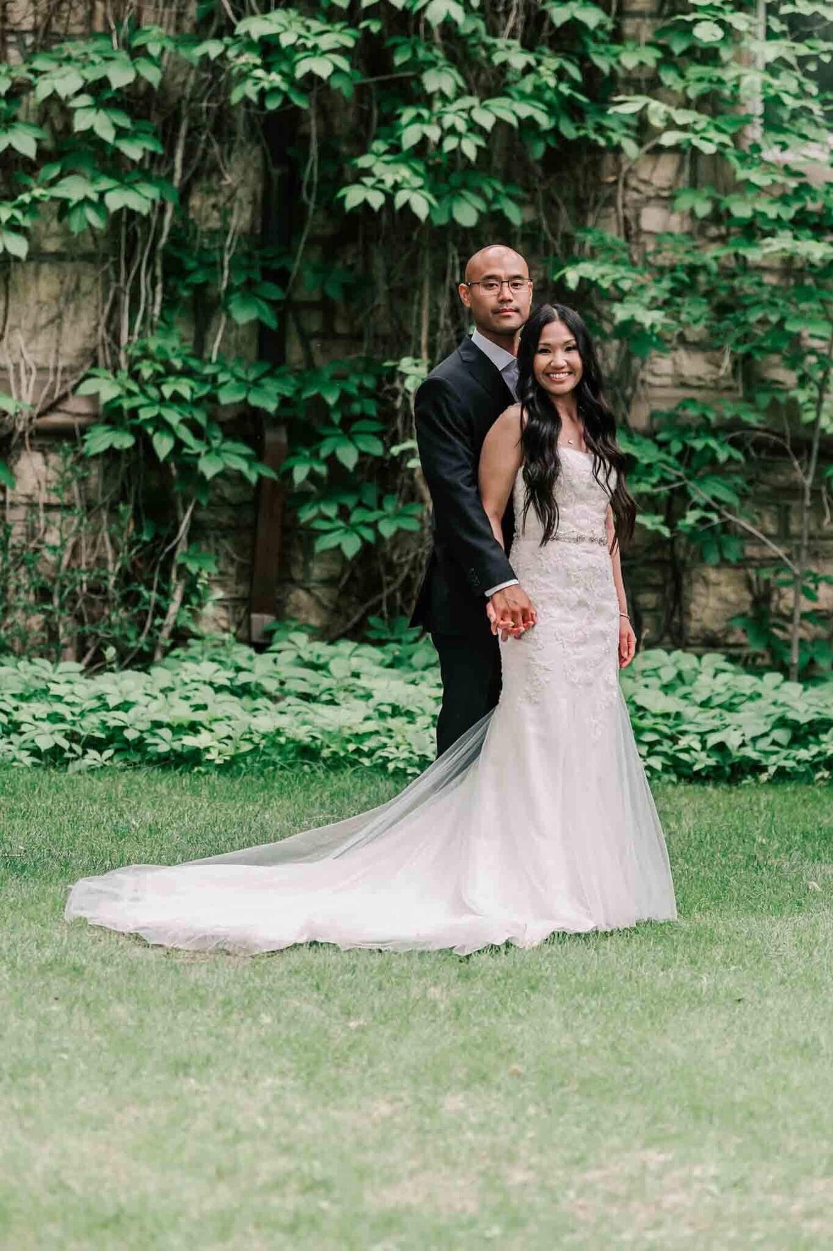 Bride standing just in front of her groom by a brick building.