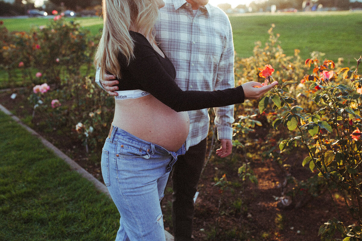 A couple walk through roses for their maternity photos
