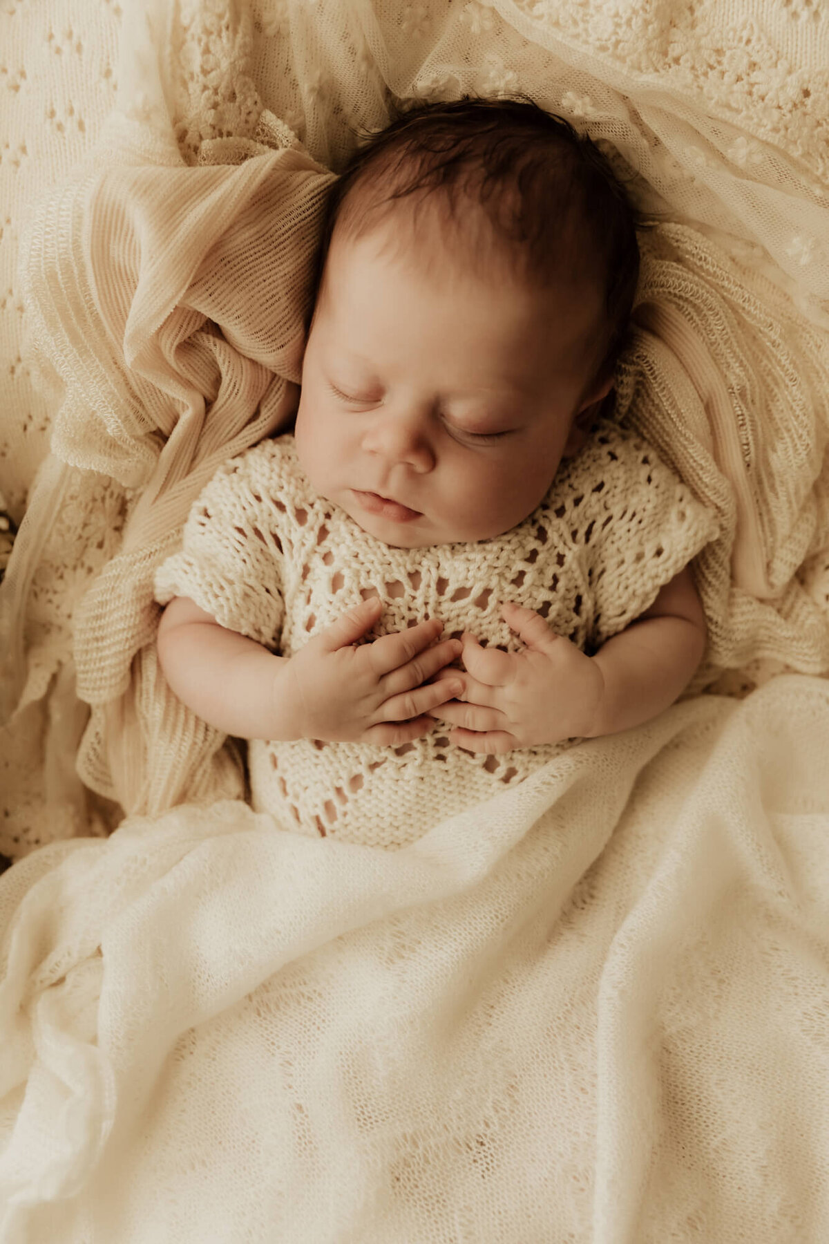 Baby girl sleeping in a basket with a cream colored blanket.
