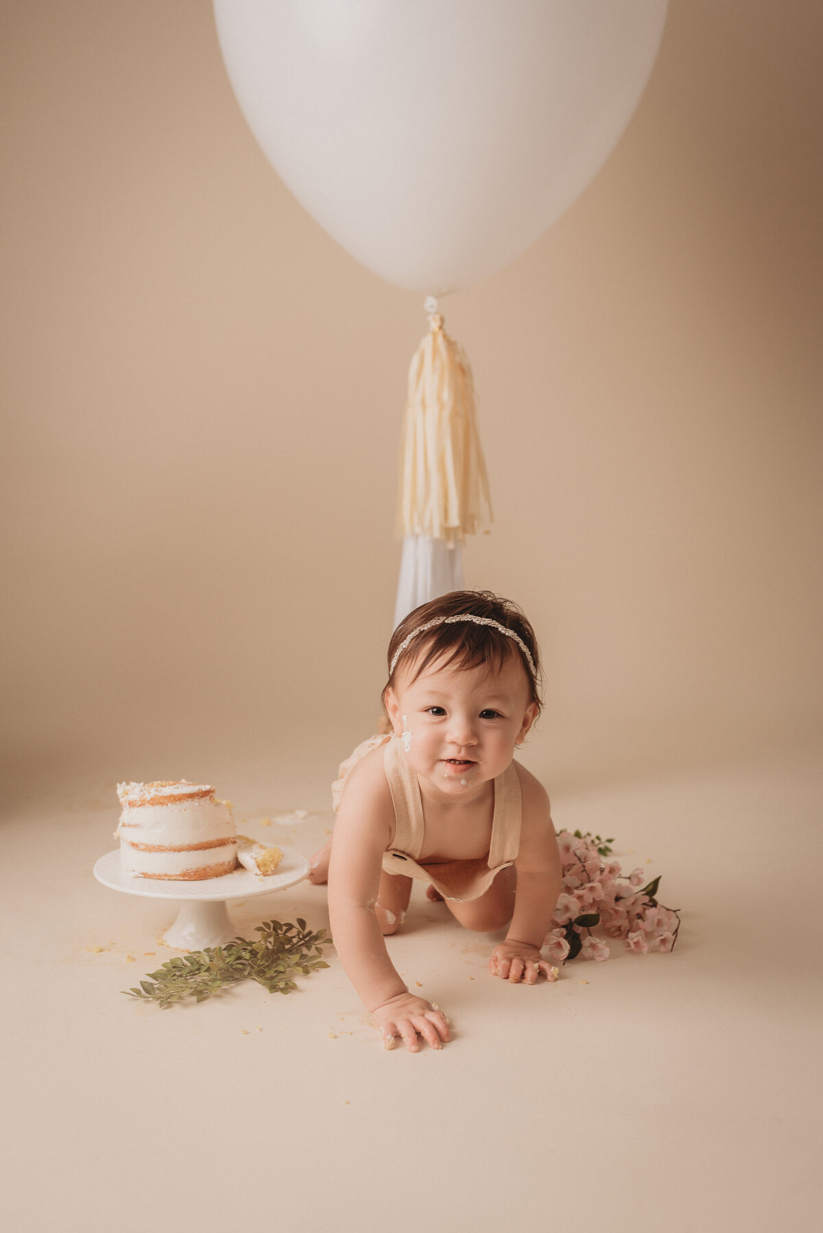 one year old baby girl with brown hair crawling towards the camera with cake next to her for cake smash birthday pictures in Atlanta GA