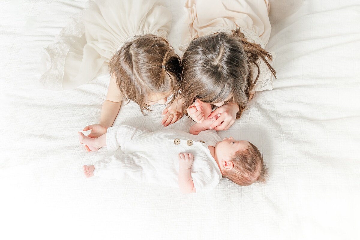 siblingsd lay on bed during in-home newborn photo session with Sara Sniderman Photography in Needham Massachusetts
