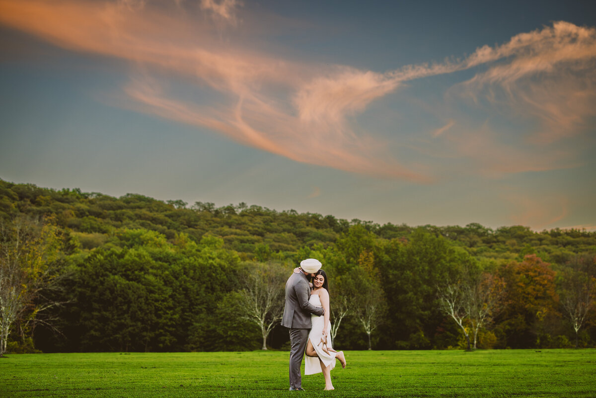 A couple standing on a field at the ringwood state park in nj with the sunset clouds in the sky