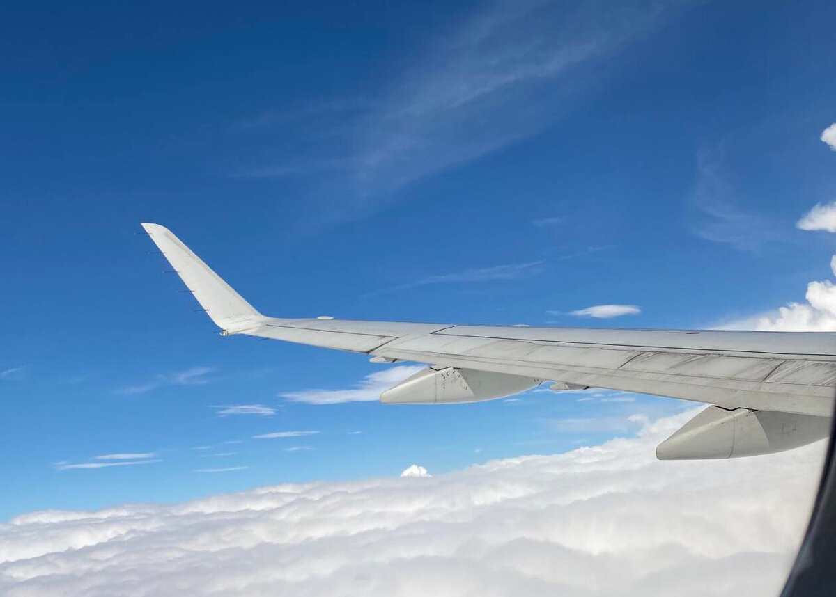 airplane wing flying through a blue sky with some clouds