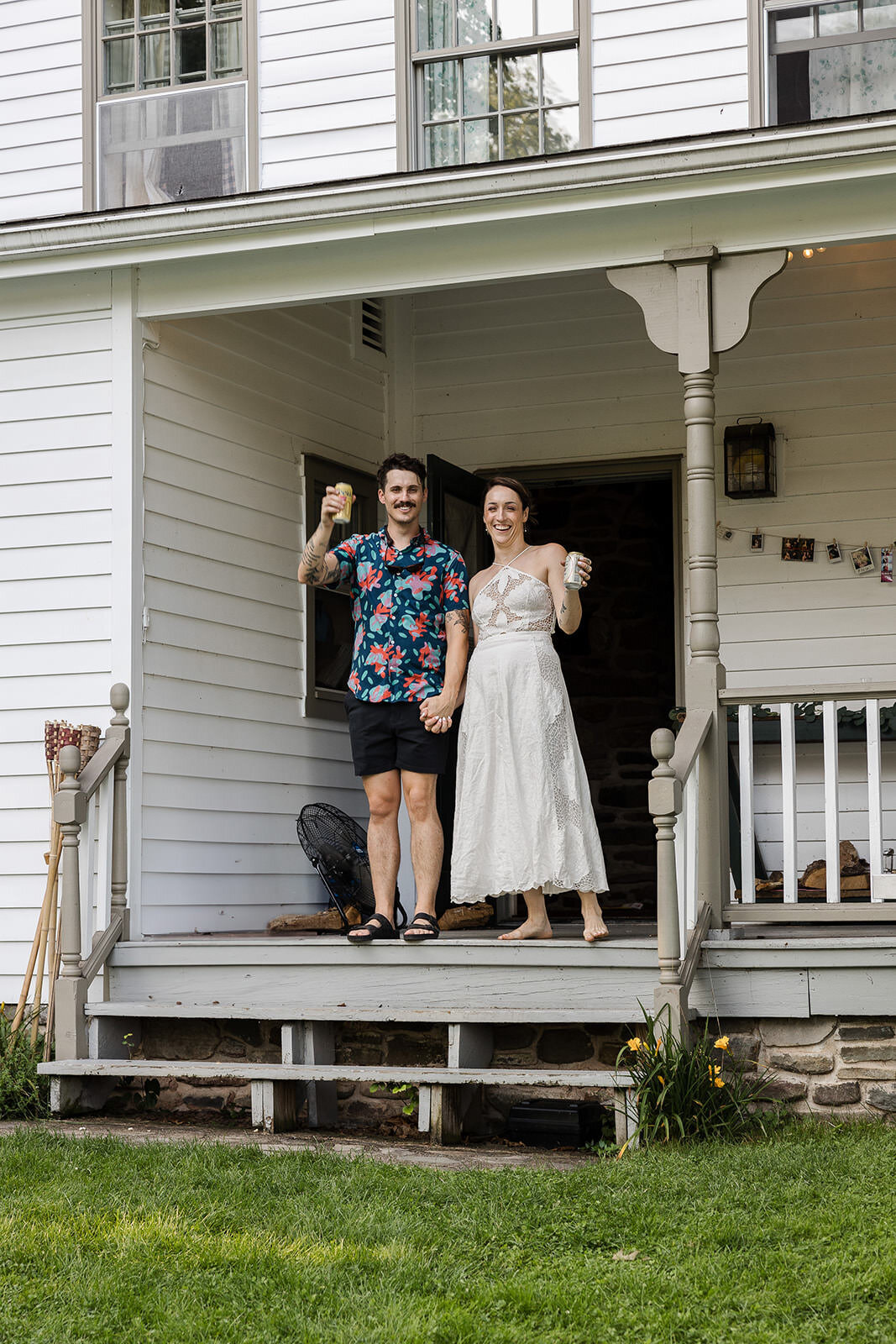 Newlyweds standing on a porch holding up beers