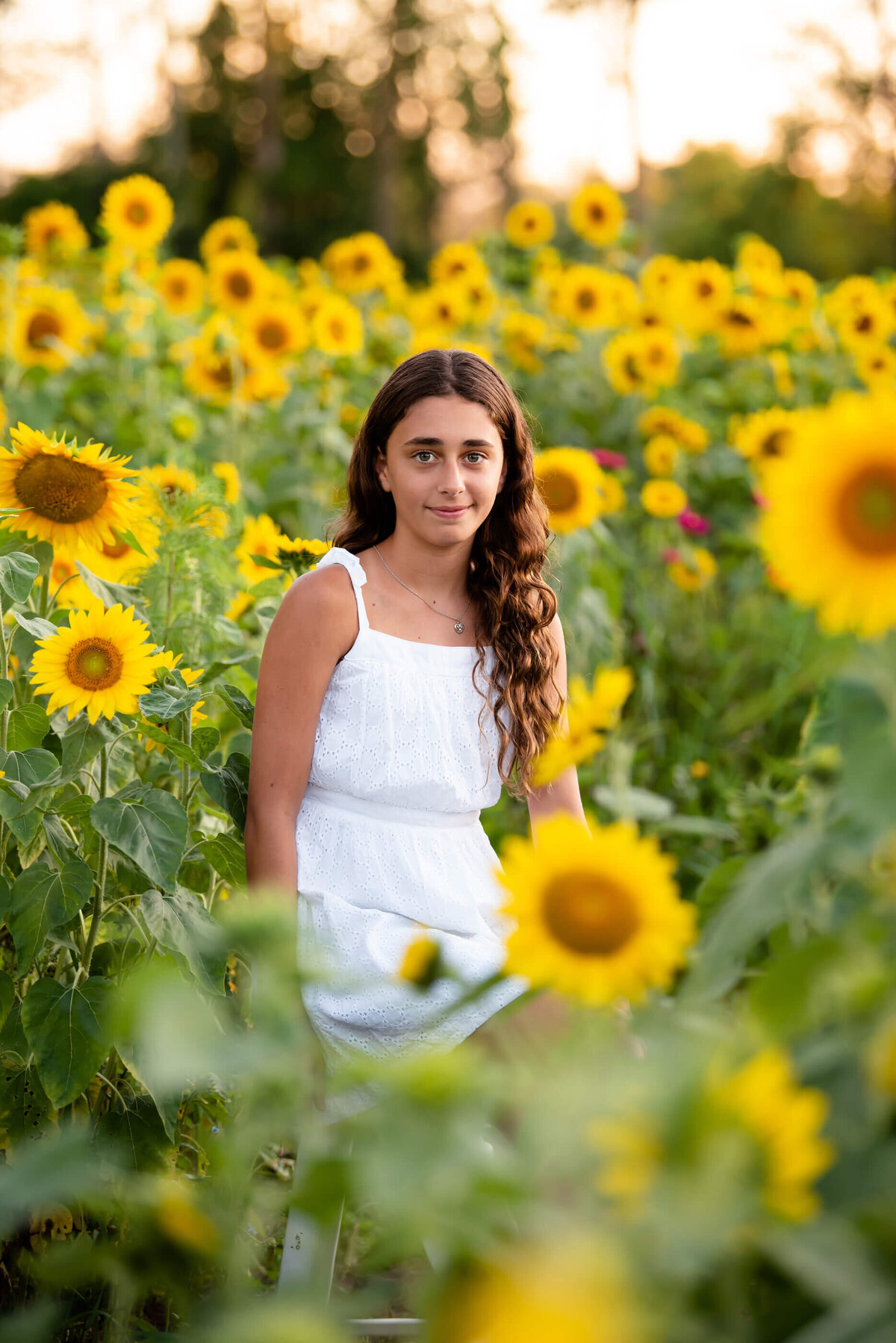 Teenage girl wearing white standing in a sunflower field for her Burlington, ON family photos 