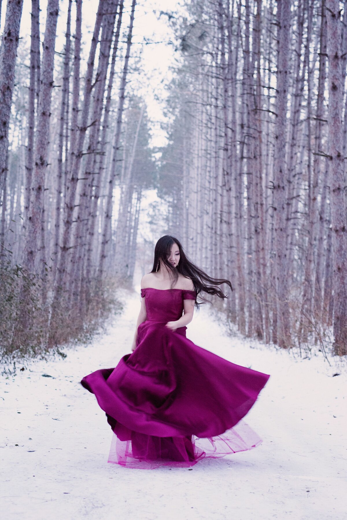 grad photo of girl in pink prom dress spinning in winter woods