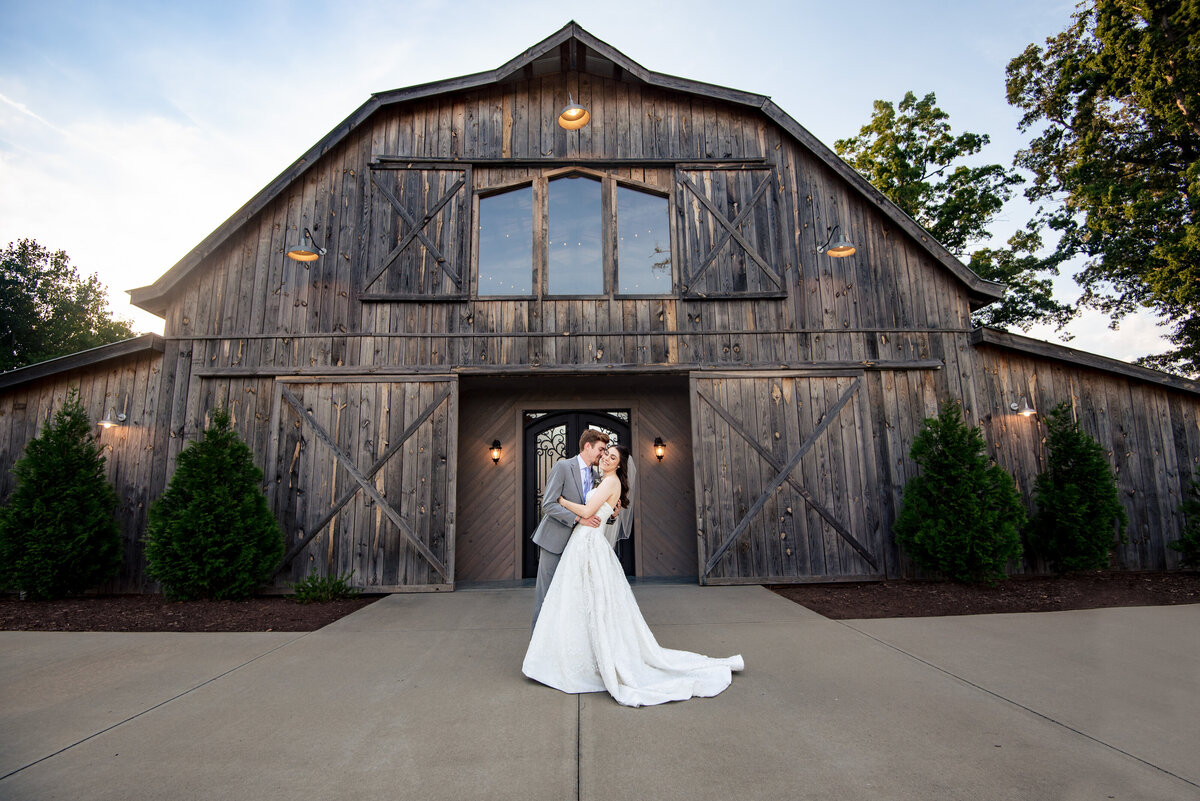 Wide and low angle photograph of a groom dipping his smiling bride in front of the barn at Lady Bird Farms by Charlotte wedding photographers DeLong Photography