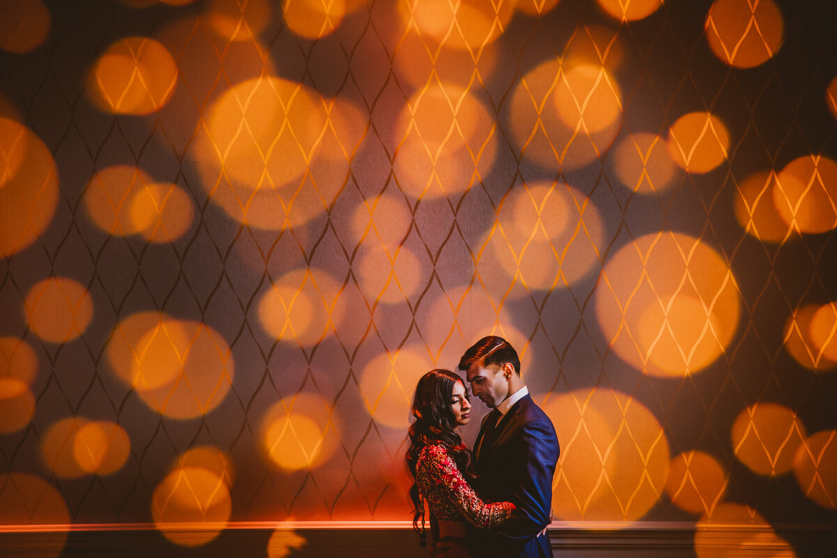 An indian bride and groom standing in front of the wall that has LED spotlights over it at the marigold nj