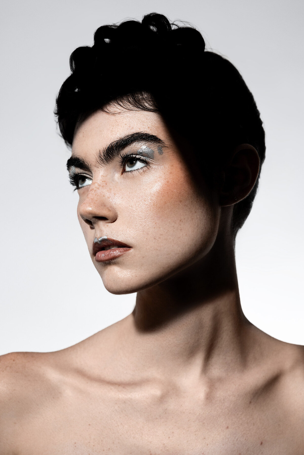 Beauty photography portrait of freckled model with silver metallic eyeshadow and artistic shadow play